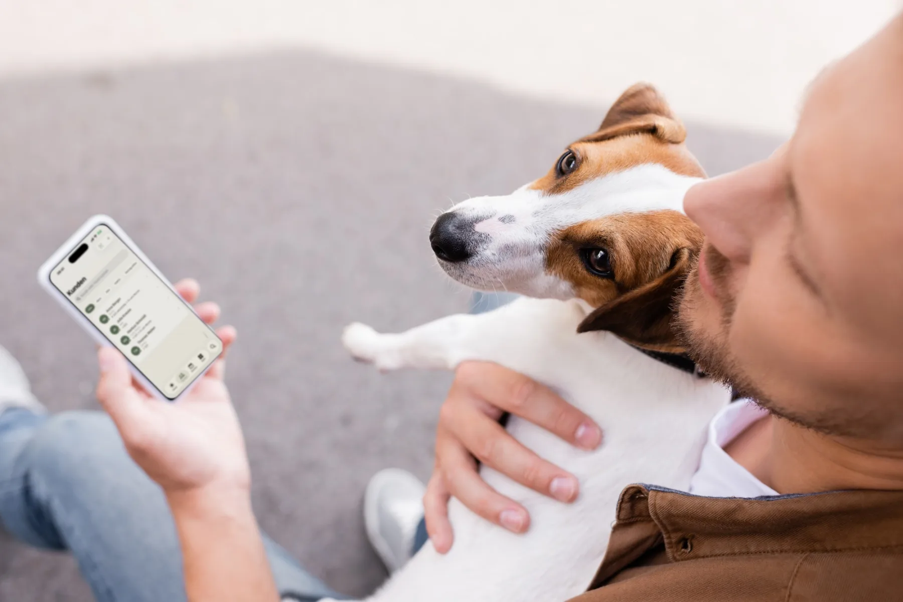 Ein Mann hält seinen Jack Russell im Arm und hat die Kundenliste von Dog Walkers auf dem iPhone geöffnet.
